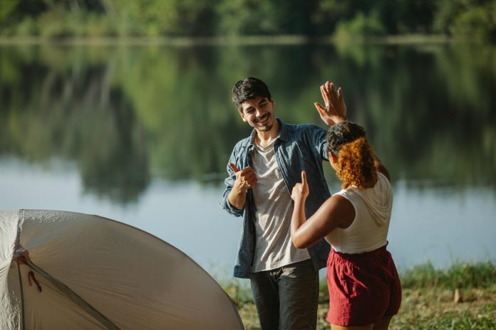 multiracial couple of travelers showing like gesture on lake coast